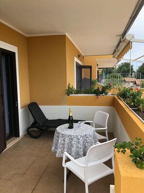 A balcony with a table and chairs, a bottle of champagne, and a view of a garden. - Residenza De Luca (Tropea)