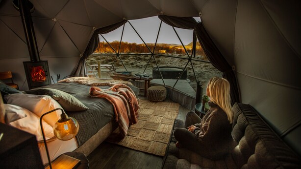 A cozy tented accommodation with a bed, seating area, and a wood-burning stove. - Reykjavik Domes (Reykjavik)