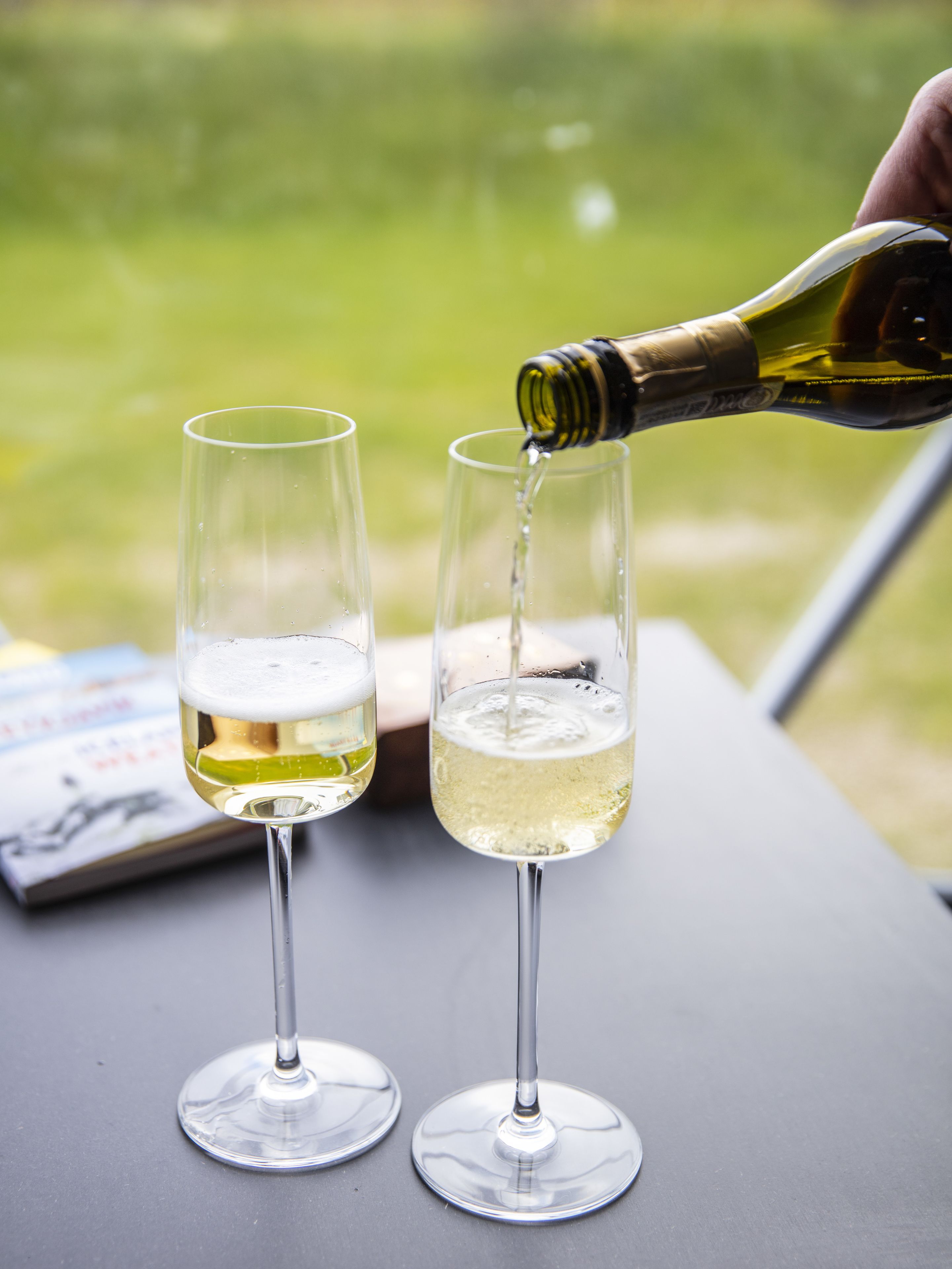 Dos copas de vino sobre una mesa, con una botella siendo vertida en una de ellas.