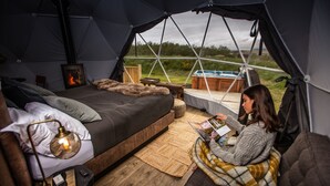 A cozy tented accommodation with a bed, reading area, and a wood-burning stove. - Reykjavik Domes (Reykjavik)