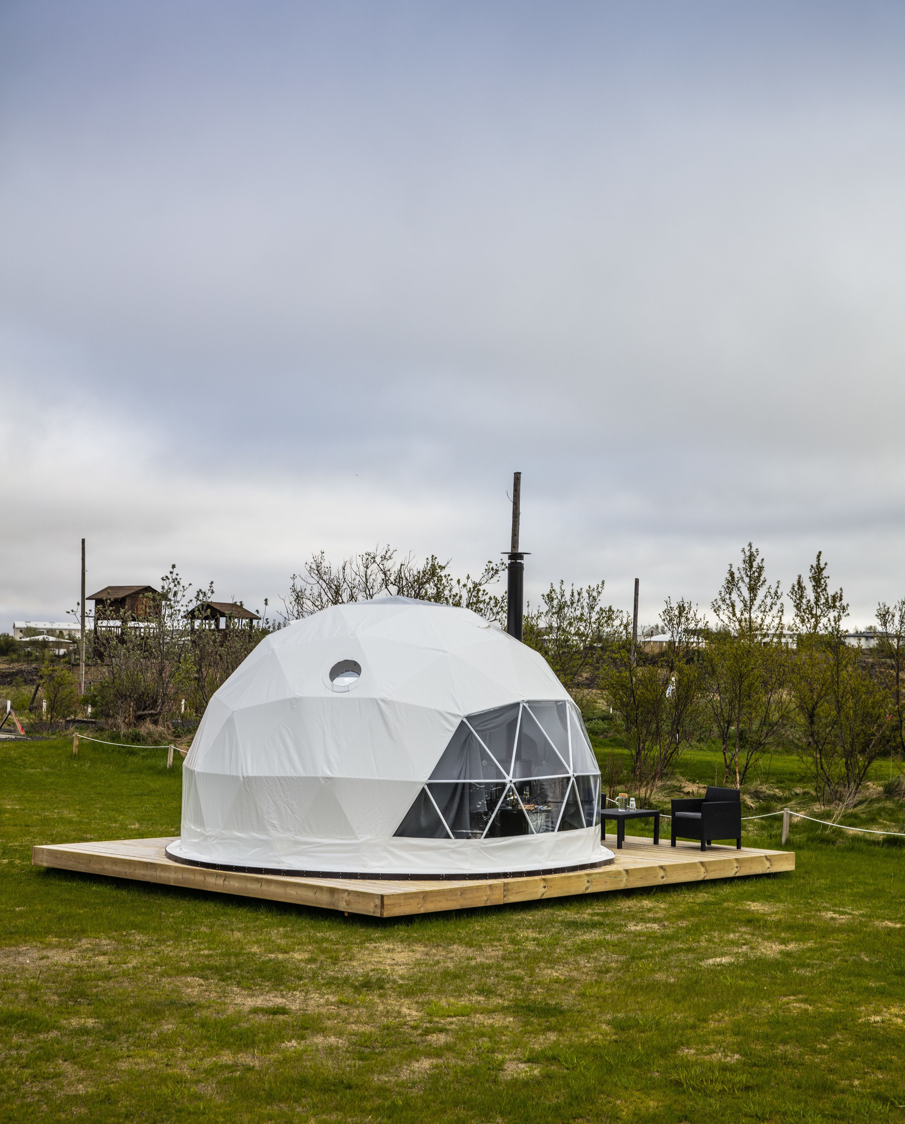A geodesic dome structure with a central skylight, a wooden platform, and a seating area with a table and chairs.