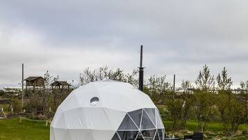 A geodesic dome structure with a central skylight, a wooden platform, and a seating area with a table and chairs.