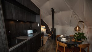 A compact kitchen with dark wood cabinets, a white countertop, and a stove. There is a dining area with a table set for four, chairs, and a potted plant. - Reykjavik Domes (Reykjavik)