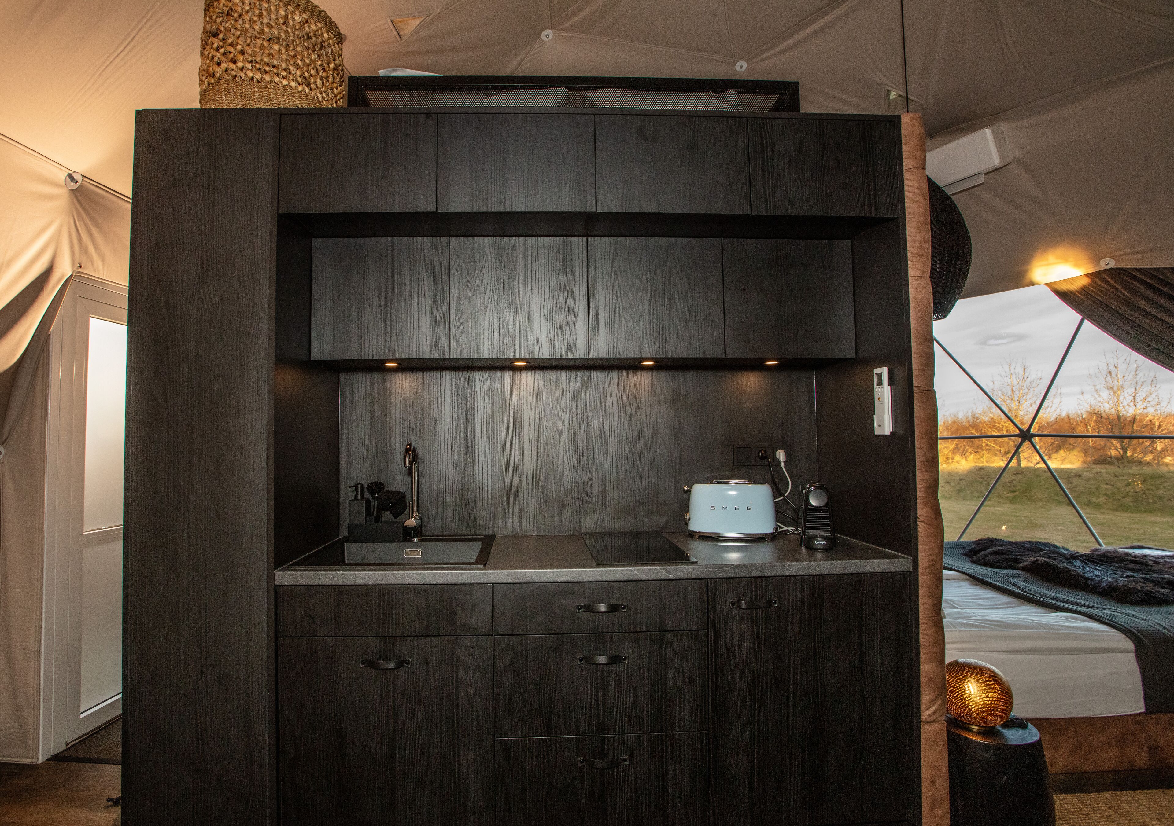 Una cocina compacta con estufa integrada, lavamanos y armarios, y una cama con vistas al exterior.