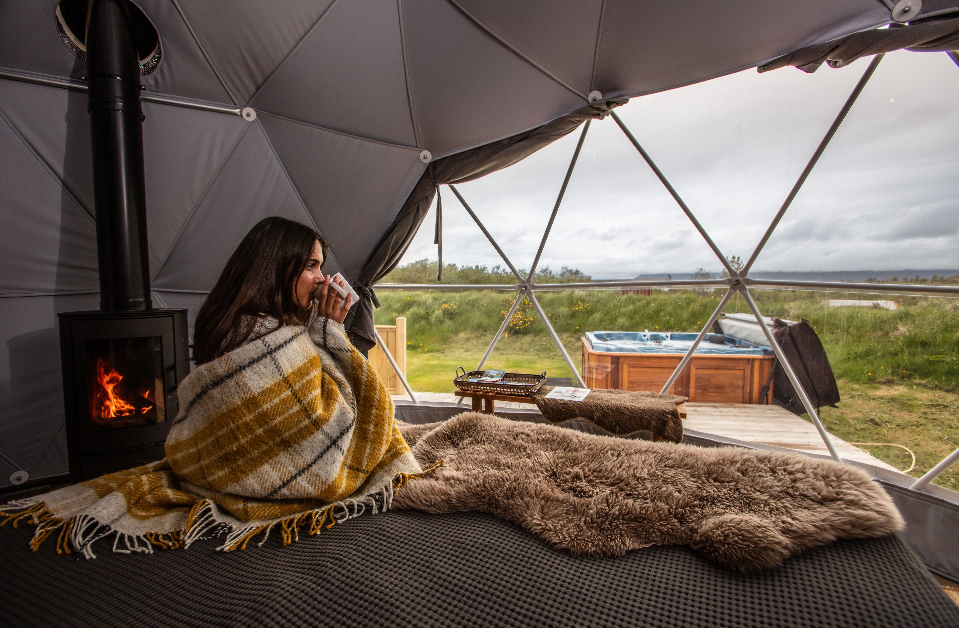 A cozy tent with a wood-burning stove, a view of the outdoors, and a hot tub.