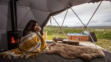 A cozy tent with a wood-burning stove, a view of the outdoors, and a hot tub.