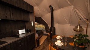 A cozy tented accommodation with a kitchenette, a dining area, and a central fireplace. - Reykjavik Domes (Reykjavik)