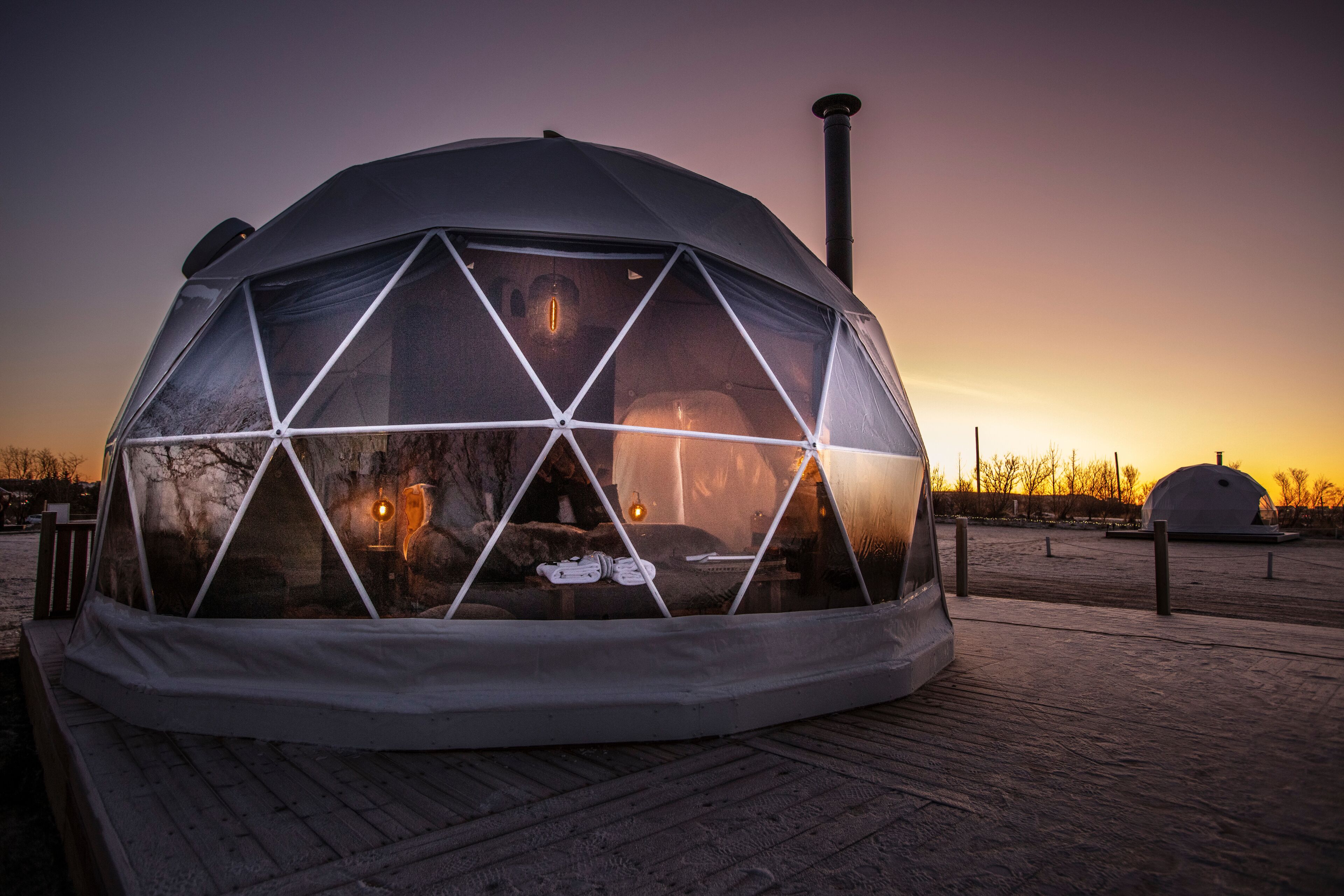 A geodesic dome structure with a transparent roof, a chimney, and a wooden deck in front.