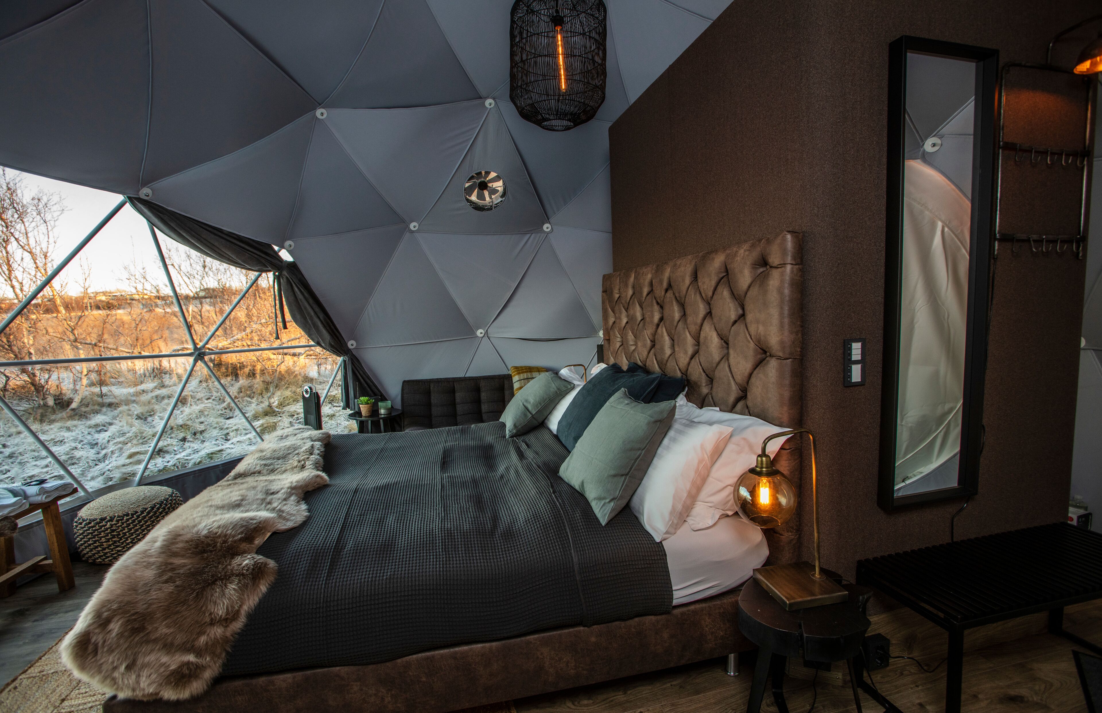 A modern bedroom with a large bed, a tufted headboard, and a view of a snowy landscape through a geometric window structure.