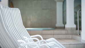 Een rij witte lounge stoelen met metalen frames, een betegelde muur en een zwembad op de achtergrond.