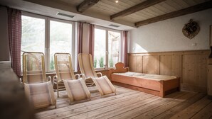Een kamer met houten vloeren, een bed, fauteuils en grote ramen voorzien van gordijnen.