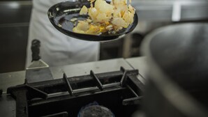 Een kok kookt in een professionele keuken met roestvrijstalen apparatuur en een modern design.