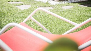 Een houten prieel met een bankje, omringd door groen en een pad van stenen.