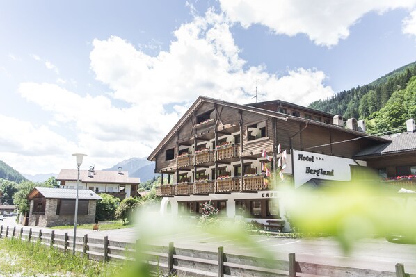 Un hôtel à plusieurs étages doté de balcons, une enseigne indiquant « Hôtel Bergland », et une vue sur les montagnes en arrière-plan.