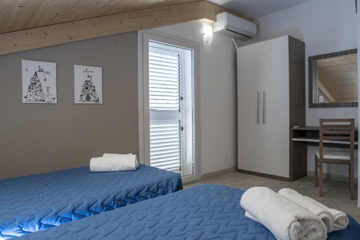 Quarto com duas camas, um guarda-roupa, uma escrivaninha e um espelho.