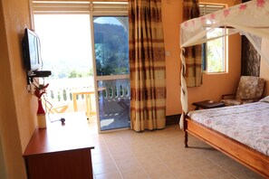 A bedroom with a wooden bed, a TV mounted on the wall, a balcony with a view of the outdoors, and a curtain. - Taita Rocks Hotel (Taita Hills)