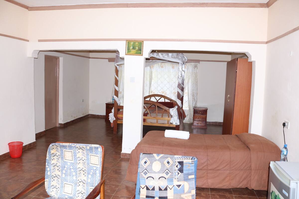 A room with a bed, two chairs, a small table, and a wall-mounted TV.