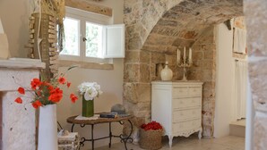 A rustic stone room with a white dresser, a small table with a vase of red flowers, and a basket of red flowers.