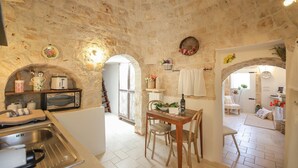 A kitchen with stone walls, a dining area with a table and chairs, and a view into another room.