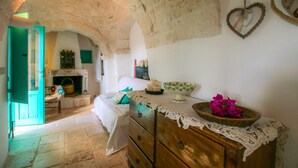 A rustic room with a stone archway, a bed with a green door, a wooden dresser, and a heart-shaped decoration on the wall. - Il Pinnacolo Verde (Alberobello)