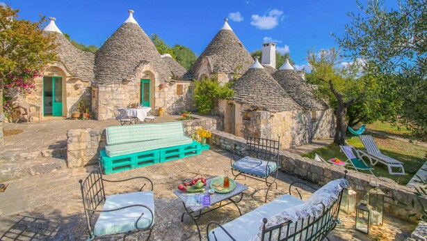 A traditional stone building with conical roofs, a patio with outdoor furniture, and a small garden area. - Il Pinnacolo Verde (Alberobello)