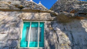 A stone building with a window featuring a turquoise frame and white shutters. - Il Pinnacolo Verde (Alberobello)
