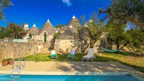 A pool area with lounge chairs and a hammock, surrounded by stone buildings with conical roofs. - Il Pinnacolo Verde (Alberobello)