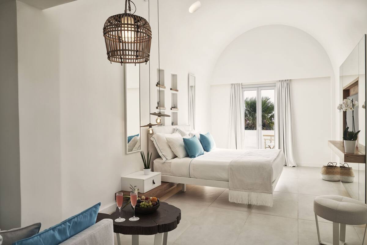 Une chambre moderne avec un grand lit, des tables de chevet, une petite table avec des boissons et une vue sur l’extérieur.