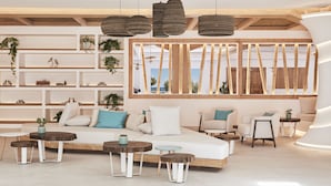 A modern interior with a wooden ceiling, white walls, and a large window with bamboo slats. There are multiple seating areas with cushions and small tables.