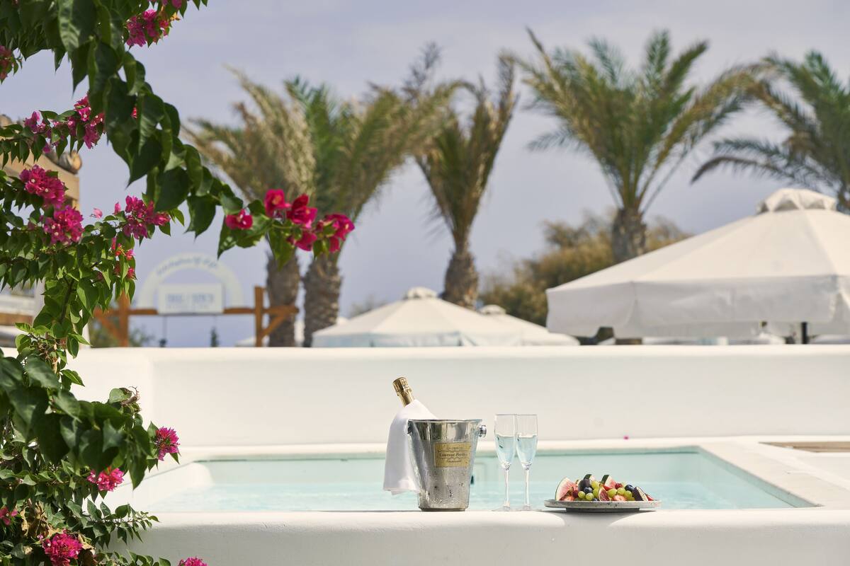 Une scène au bord de la piscine avec une bouteille de champagne, deux verres et une assiette de fruits.