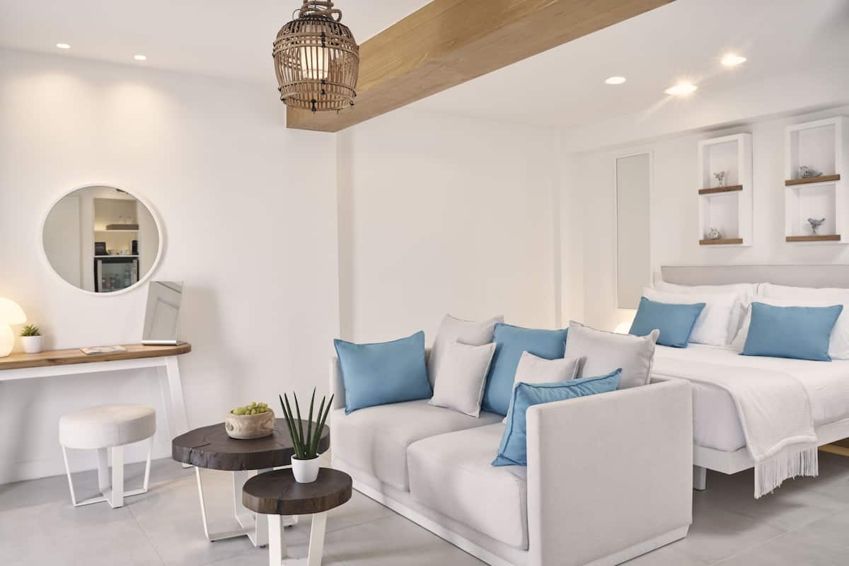 Une chambre moderne aux couleurs neutres, avec des tons de blanc et de gris, comprenant un canapé, un lit, une table de chevet et un miroir.