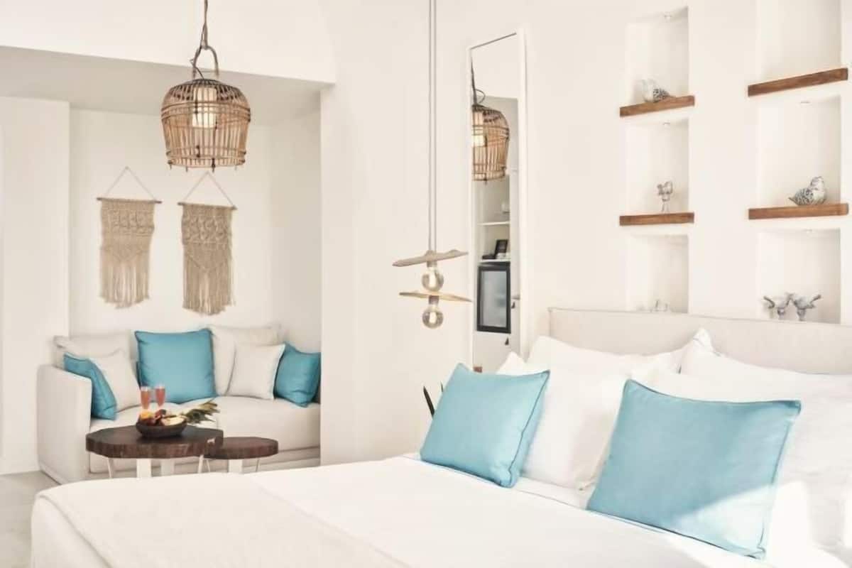 Une chambre d’hôtel moderne comprenant un lit, un canapé, une petite table avec des boissons, un luminaire suspendu et un miroir.