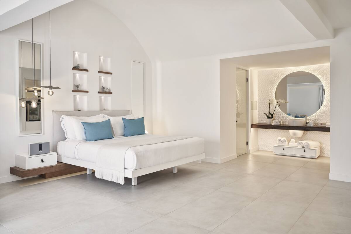 Une chambre à coucher moderne avec un lit, des tables de chevet, un miroir et une coiffeuse agrémentée d’un miroir rond.