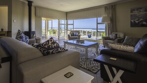 A spacious living area with a view of the ocean, furnished with a sofa, armchairs, and a coffee table. - Home with an Ocean view (Hermanus)