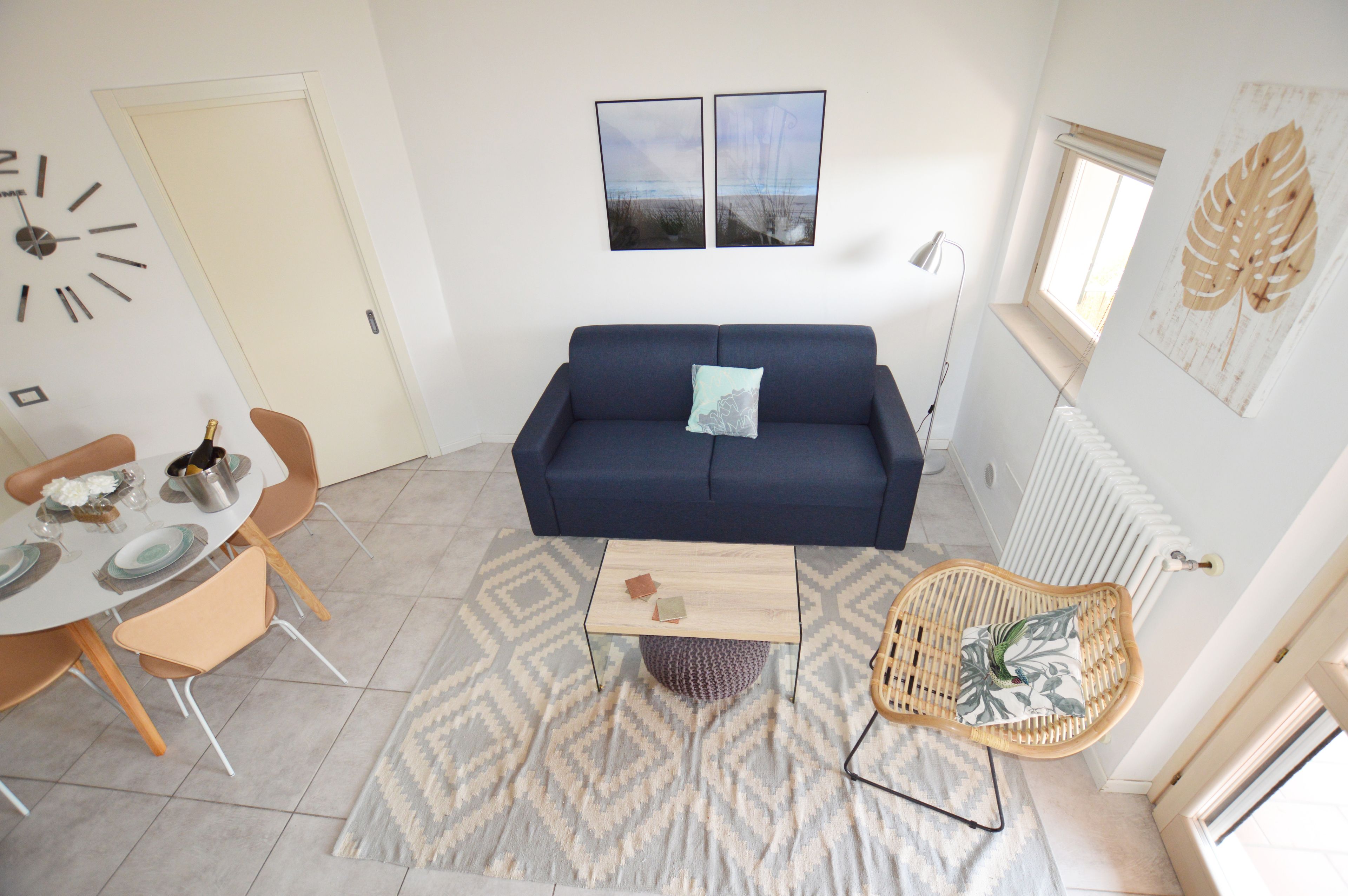 A living room with a blue sofa, a round coffee table, a dining table with chairs, and a decorative wall clock.