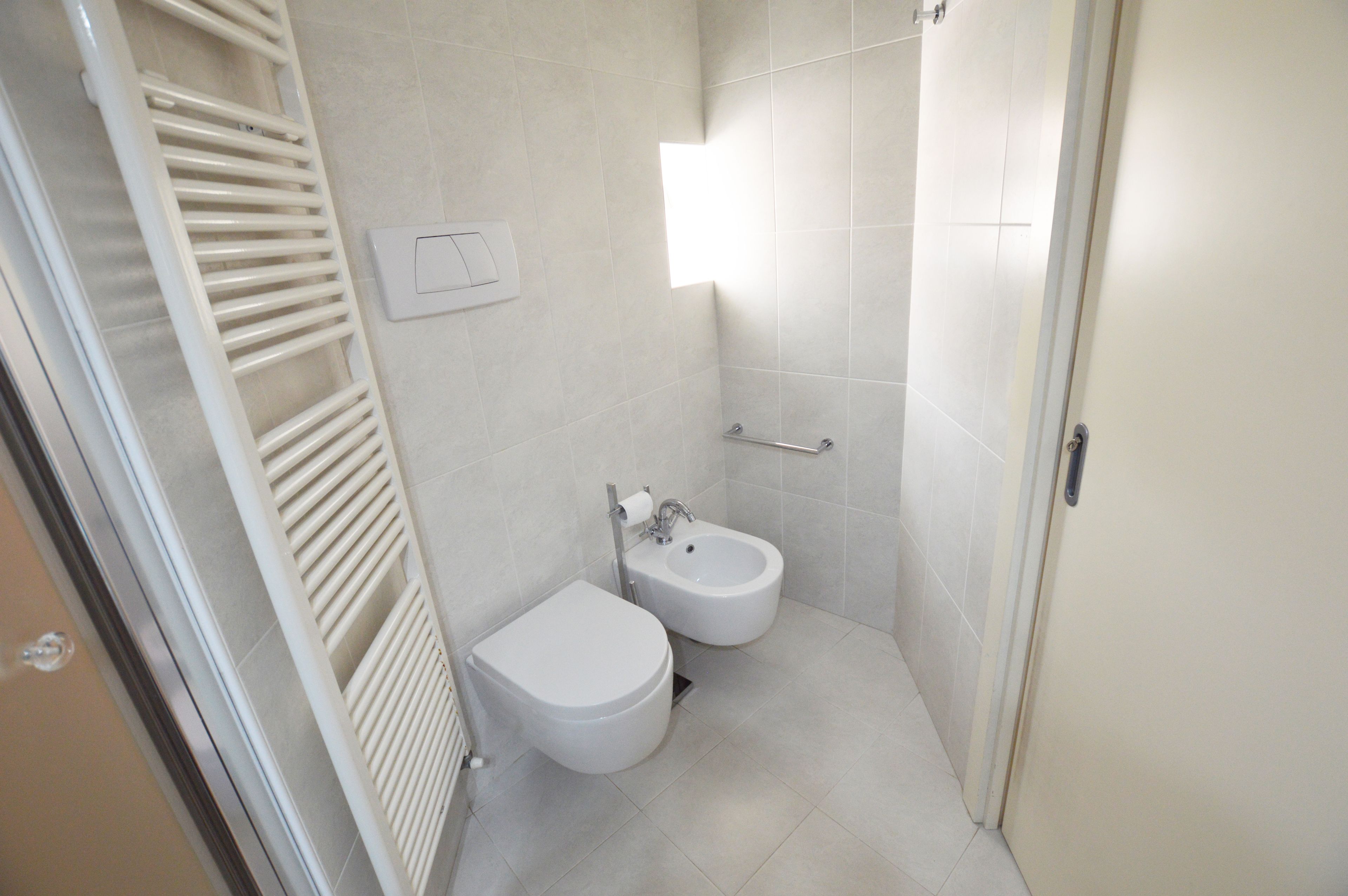 A small, clean bathroom with a toilet, bidet, and towel rack.