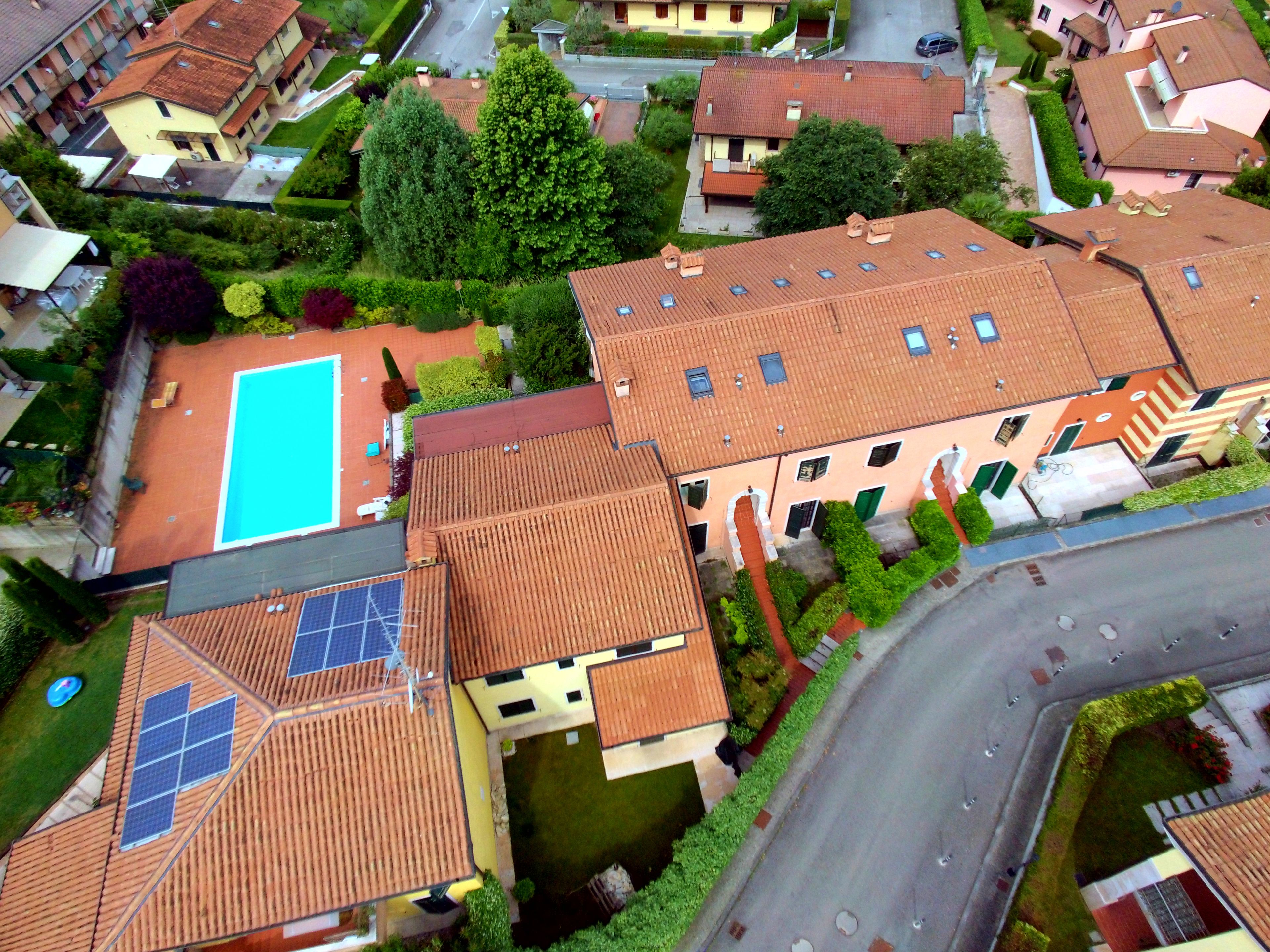 An aerial view of a residential area with multiple houses, a swimming pool, and solar panels on rooftops.