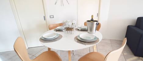A dining area with a round table, two chairs, a clock on the wall, and a bottle of champagne.