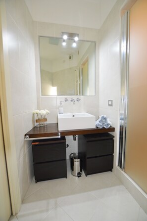 A bathroom with a white sink, a mirror above it, and a dark wooden countertop. There are two black drawers below the sink and a trash can to the right. - Salionze - Via Benaco 80 (Valeggio sul Mincio)