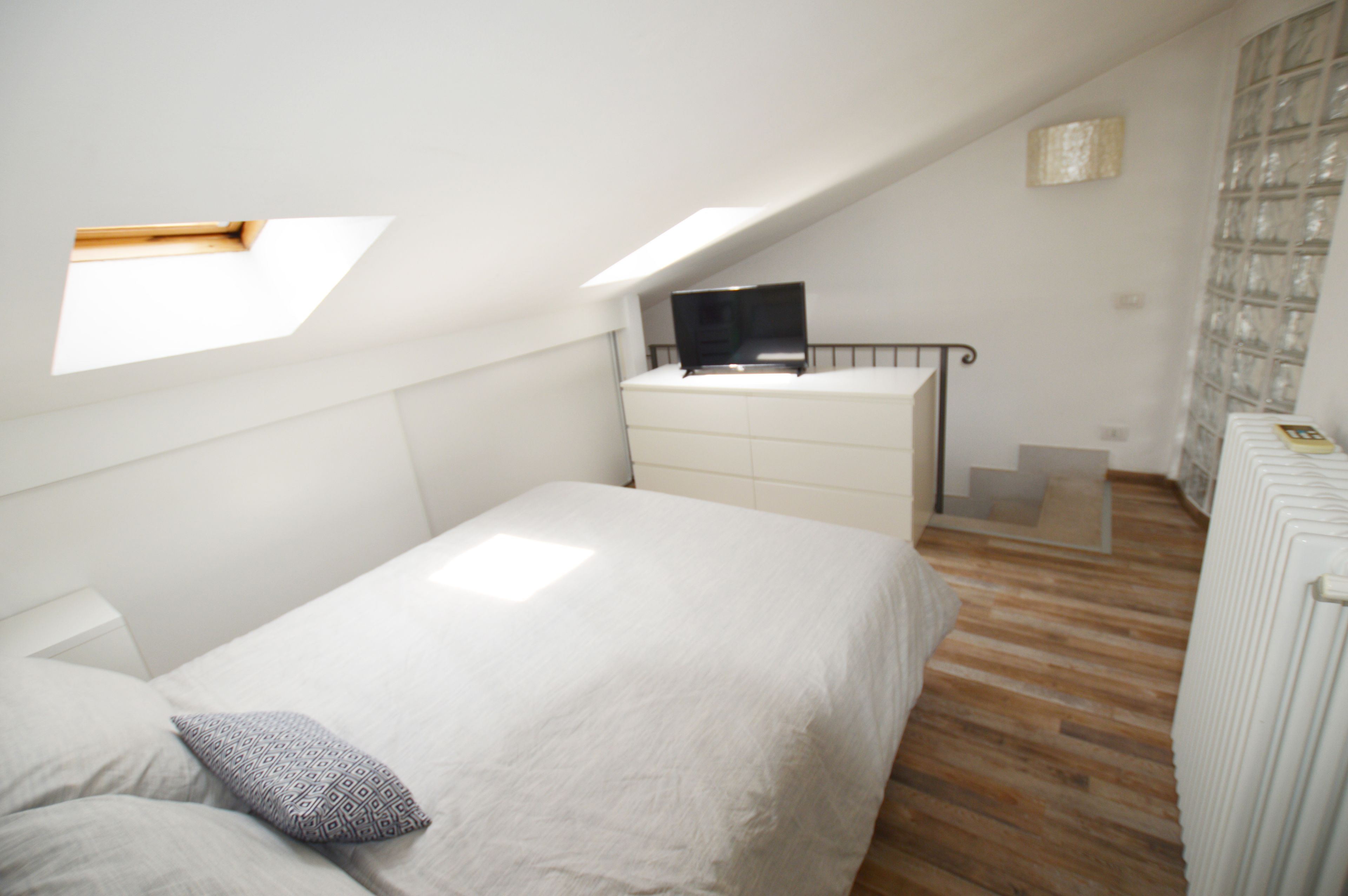 A bedroom with a bed, a dresser, a TV on a stand, and a skylight.