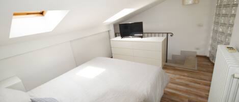 A bedroom with a bed, a dresser, a TV on a stand, and a skylight.