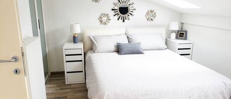 Un dormitorio con una cama grande, dos mesitas de noche, un radiador y espejos decorativos en la pared.