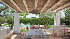 Un patio al aire libre con una mesa y sillas, un banco de piedra y una lámpara colgante.