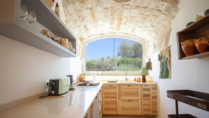 Una cocina con arco de piedra, armarios de madera, una ventana con vistas y un estante con utensilios de cocina.
