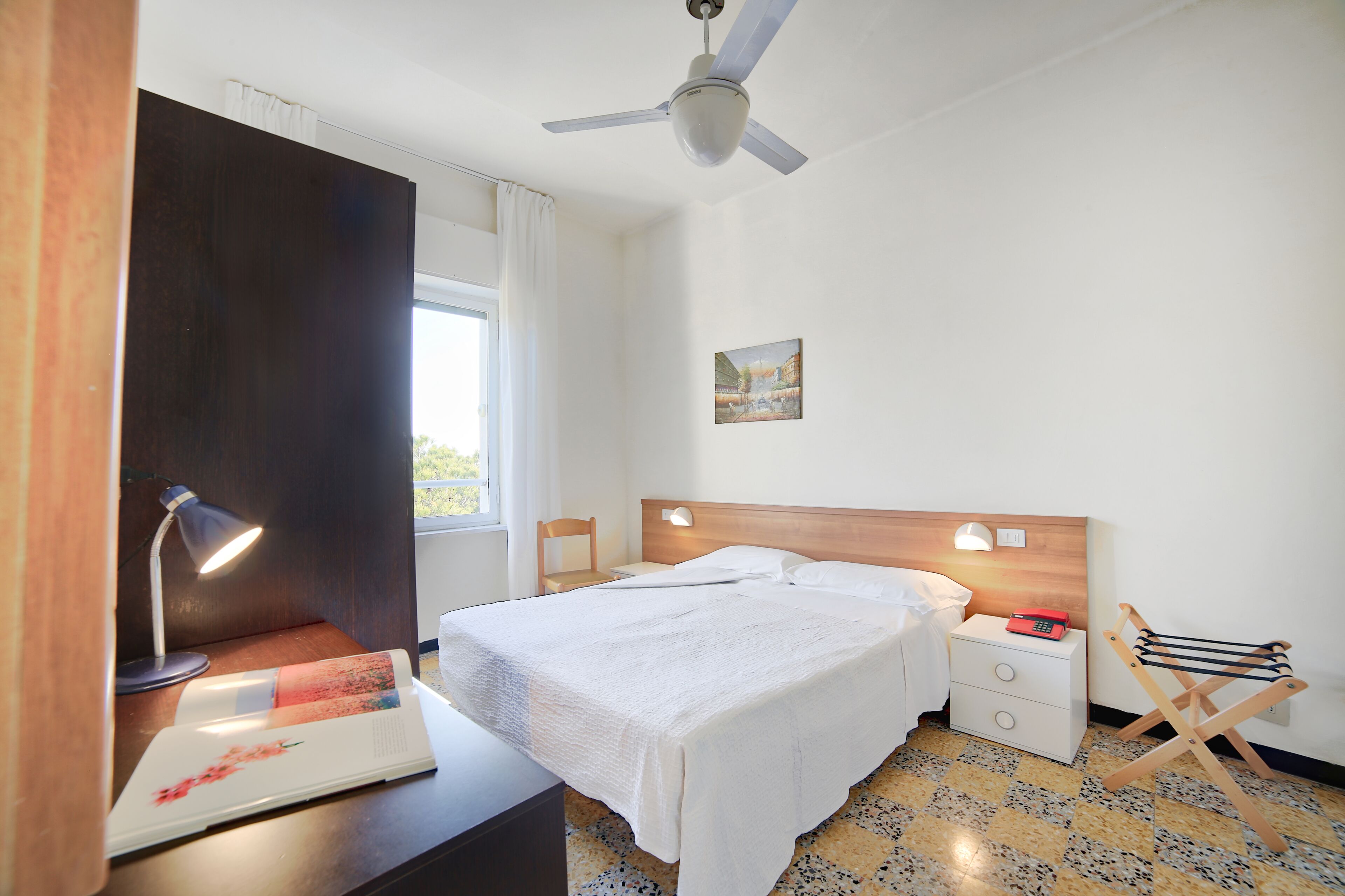 Une chambre d’hôtel bien rangée, avec un lit, des lampes de chevet, un bureau avec une lampe, une chaise et une petite table.