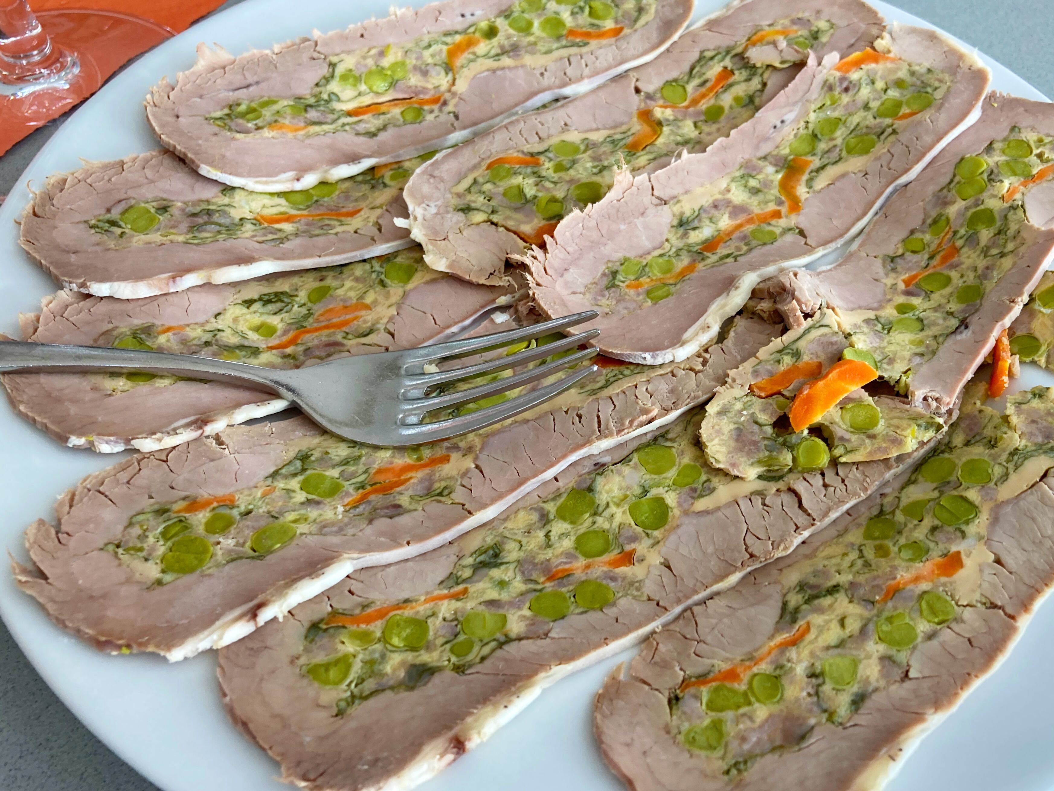Une assiette de tranches de pain de viande, accompagnée de petits pois et de carottes.