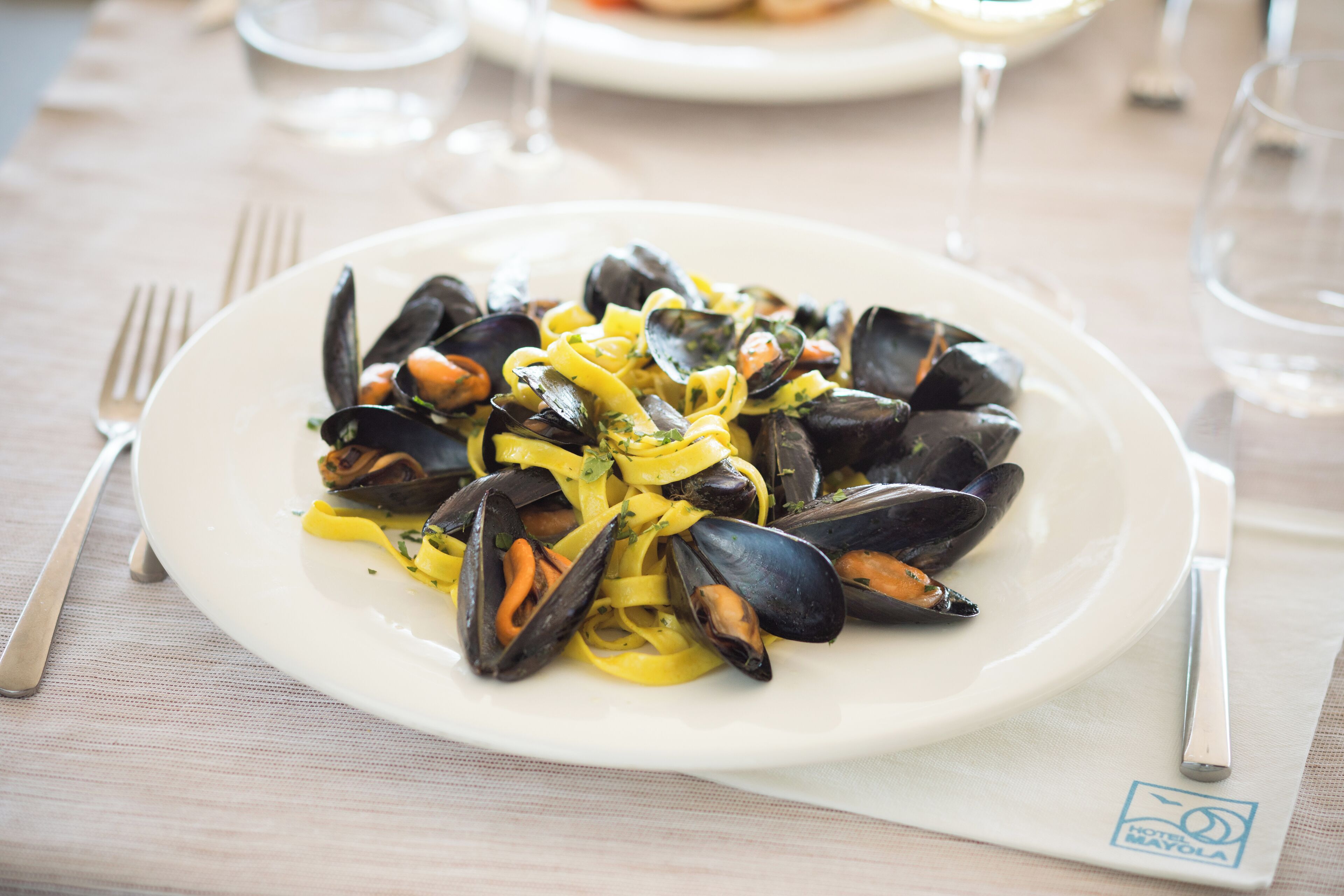 A plate of mussels with pasta on a white plate, set on a table with a placemat and cutlery.