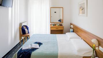 Una camera d'albergo con un letto, un comodino, uno specchio, una TV a parete e una finestra con tende.