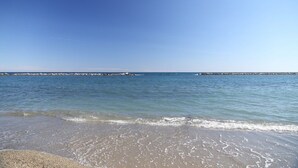 Una playa con agua cristalina, un rompeolas rocoso y un mar tranquilo.