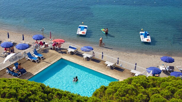 Un área de piscina con sillas de descanso y sombrillas, una terraza de madera y vista al mar.